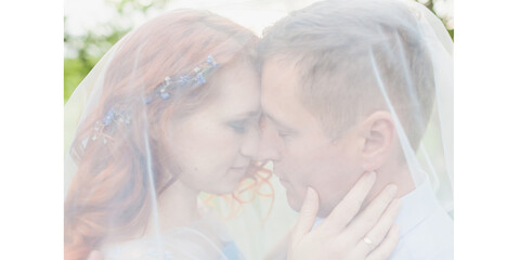 young couple in love kissing under a veil. woman with fiery hair in a blue dress. photo shoot in an apple orchard