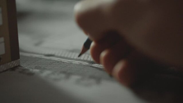 Design work takes place in the office of an architectural firm. A white man carefully uses a pencil to create blueprints of a building. Design engineer working on sustainable building concept