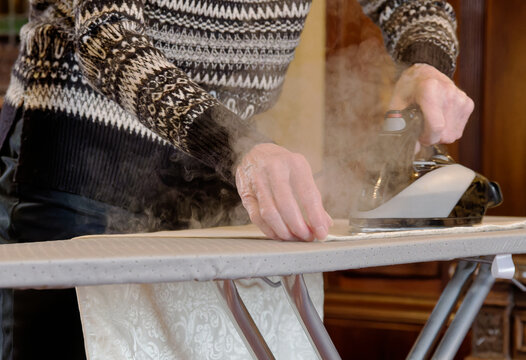 Elderly woman ironing clothes with electric iron