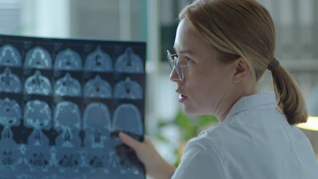 Female doctor examining x-ray image and commenting on diagnosis when giving health consultation to patient in medical office