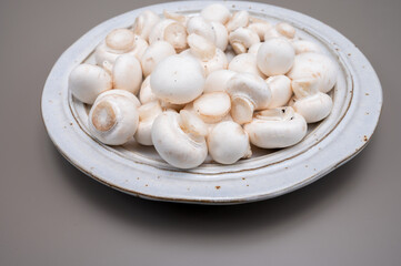 Fototapeta na wymiar White champignon mushrooms fresh uncooked on white ceramic plate copy space