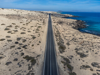 Fototapeta premium Driving car on black asphalt road through white sandy dunes near Corralejo beach at colorful sunset Fuerteventura, Canary islands, Spain