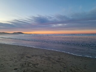 Sunset on Famara Beach, Lanzarote, casts a mesmerizing palette of colors across the sky, blending hues of orange, pink, and purple against the backdrop of the Atlantic Ocean waves.