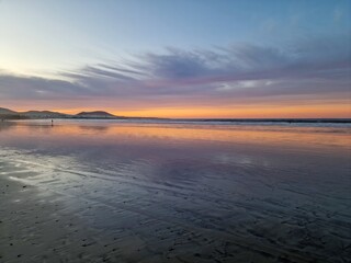 Sunset on Famara Beach, Lanzarote, casts a mesmerizing palette of colors across the sky, blending hues of orange, pink, and purple against the backdrop of the Atlantic Ocean waves.