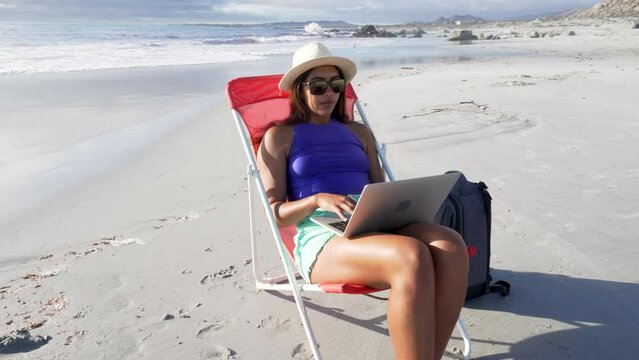 latin american digital nomad woman sitting alone on the beach doing remote work on her laptop	
