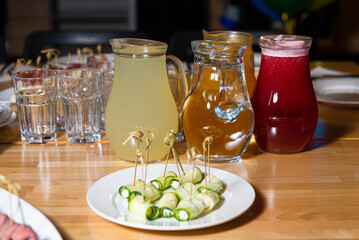 Colorful Beverage Pitchers and Cucumber Appetizers. Three pitchers filled with colorful beverages alongside a plate of cucumber roll appetizers on a wooden table.