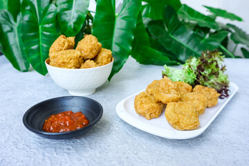 Bakso Goreng or Fried Chicken Ball, served with tomato or chili sauce on table with green foliage in the background