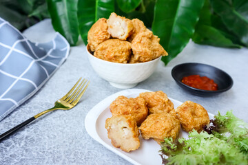 Bakso Goreng or Fried Chicken Ball, served with tomato or chili sauce on table with green foliage in the background