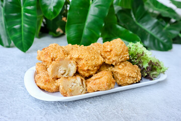 Bakso Goreng or Fried Chicken Ball, served with tomato or chili sauce on table with green foliage in the background