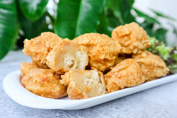 Bakso Goreng or Fried Chicken Ball, served with tomato or chili sauce on table with green foliage in the background