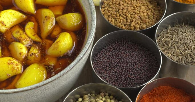 Garlic pickle, side dish from India. Around the bowl with pickled garlic are containers with spices used for pickling and squeezed lemons. Zoom in while rotating;