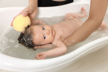 Mother bathing her little baby with sponge in bathtub, closeup