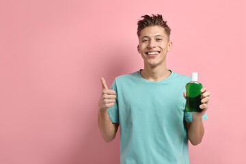 Young man with mouthwash showing thumbs up on pink background, space for text