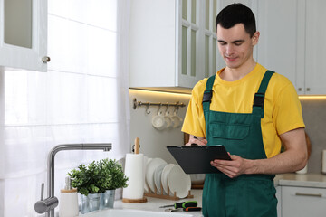 Smiling plumber with clipboard near faucet in kitchen