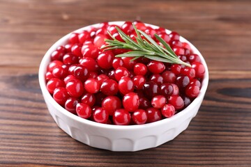 Fresh ripe cranberries and rosemary in bowl on wooden table, closeup