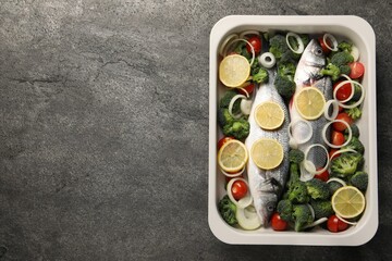 Fototapeta na wymiar Raw fish with vegetables and lemon in baking dish on grey textured table, top view. Space for text