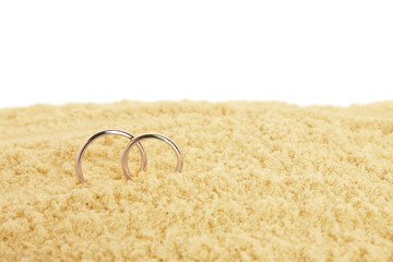 Honeymoon concept. Two golden rings and sand isolated on white