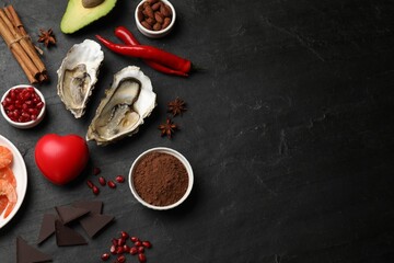 Natural aphrodisiac. Different food products and heart model on black table, flat lay. Space for...