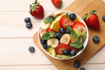 Tasty fruit salad in bowl and ingredients on wooden table, flat lay. Space for text