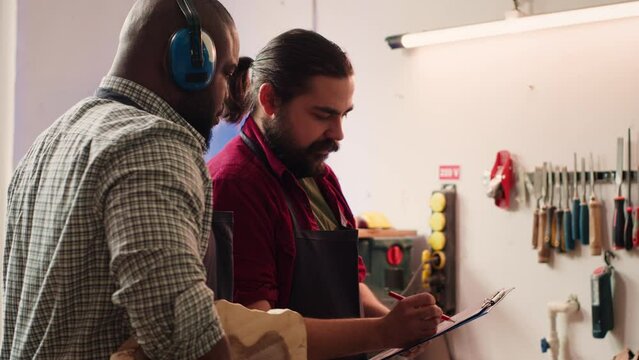Carpenter and colleague looking over technical schematics, brainstorming ideas for wooden object. Master and apprentice analyzing blueprints to execute furniture assembling project, camera A