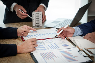 A professional businessman in a suit conducts a meeting at a desk while showcasing a model of a...