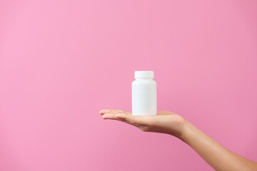 A woman hands delicately hold a bottle of medicine, isolated against pink background, depicting care, health, and the importance of pharmaceutical treatment in healthcare.
