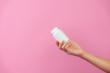 A woman hands delicately hold a bottle of medicine, isolated against pink background, depicting...