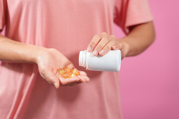 A professional image showcasing a female hand delicately holding a bottle of cod liver oil with her fingers against a soft pink isolated background.