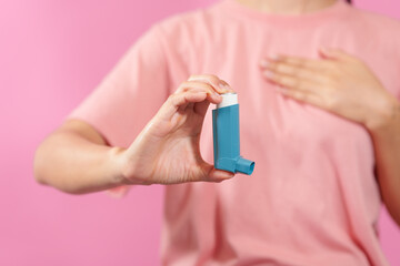 A professional image featuring a female hand holding an asthma inhaler with fingers against a soft pink isolated background, highlighting respiratory health and wellness. - obrazy, fototapety, plakaty