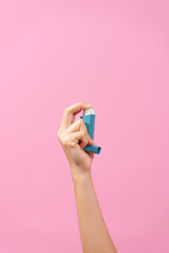 A professional image featuring a female hand holding an asthma inhaler with fingers against a soft pink isolated background, highlighting respiratory health and wellness.
