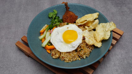 Soy sauce fried rice with chicken thigh meat, sunny side up egg, pickles, basil and emping, typical Indonesian food