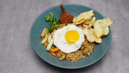 Soy sauce fried rice with chicken thigh meat, sunny side up egg, pickles, basil and emping, typical Indonesian food