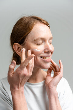 A woman applies cream to her face