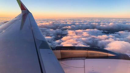 Sunset hues bathe the clouds as seen from an airplane's wing.