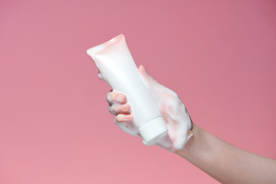 Female hands in foam with white plastic tube on pink background
