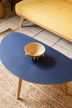 Blue coffee table with a bowl on top in front of a yellow couch
