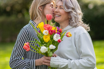 Daughter hugs mother, focus on tulip bouquet