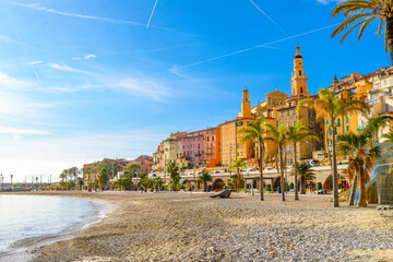 The sandy Plage des Sablettes beach and promenade, with the colorful old town and the towers of Basilica of Saint Michel behind, along the French Riviera at Menton, France. - obrazy, fototapety, plakaty