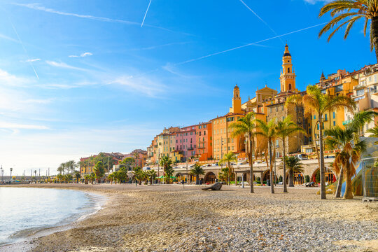 The sandy Plage des Sablettes beach and promenade, with the colorful old town and the towers of Basilica of Saint Michel behind, along the French Riviera at Menton, France.