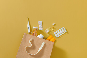 Shopping bag with different pills and thermometer on yellow background