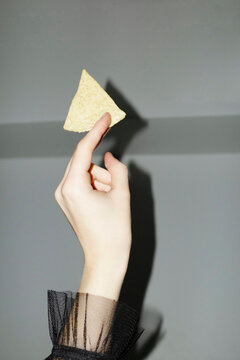 Hand with elegant ruffled mesh shirt holding chip/crisp/salty snack 