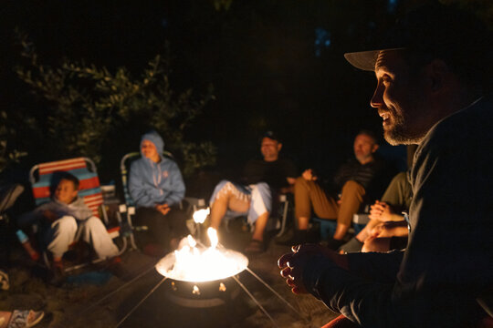 Man smiling around campfire with friends and family.