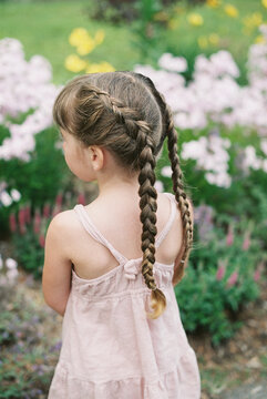 little girl with dutch braids in pink dress in flower garden in summer