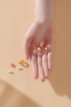 Close up of a woman's hand holding multiple pills on beige background