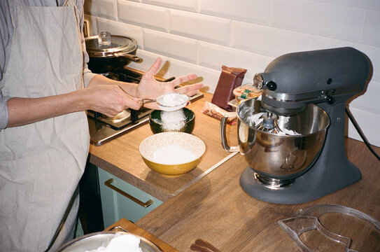 Young anonymous woman sifting flour in the kitchen at home