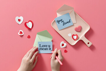 Female writing LOVE U MEAN IT note on pink background, Valentine's day