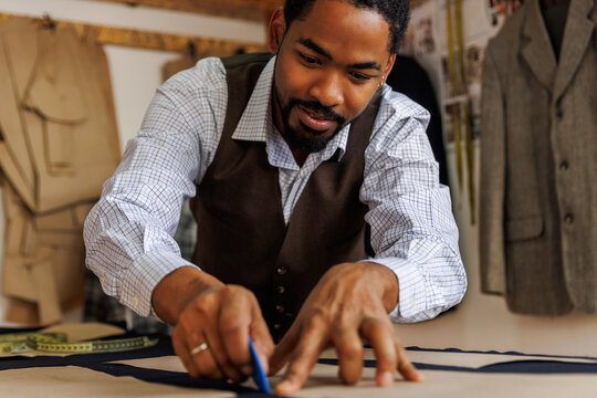 Confident designer outlining fabric at table in workshop