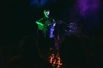 A young man is playing a song on the guitar by the fire