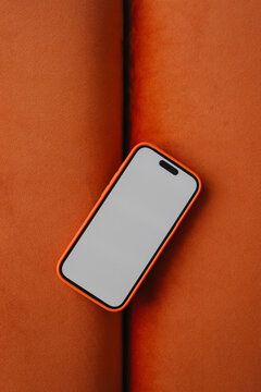 Smartphone with blank screen kept on orange cotton sofa
