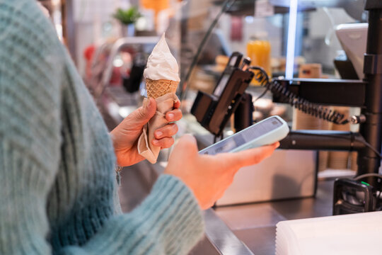 Cropped image of woman holding ice cream cone and using smartphone